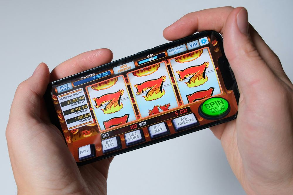 Tangan memegang ponsel dengan tampilan permainan slot mobile