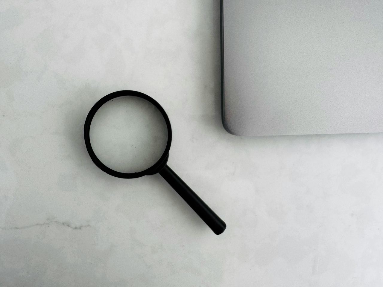 Kaca pembesar di atas meja kerja laptop, melambangkan kebiasaan memeriksa informasi secara teliti